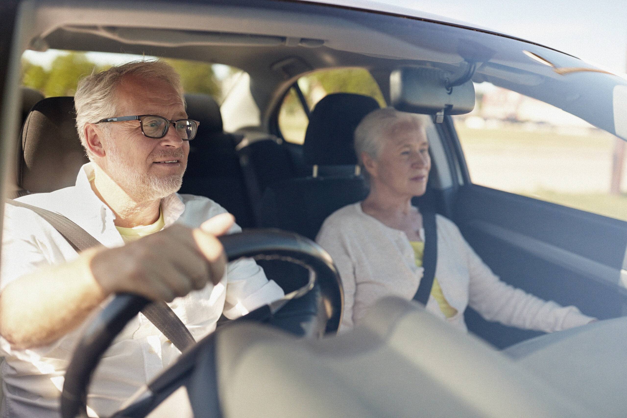 An elderly couple in a car, the man is driving