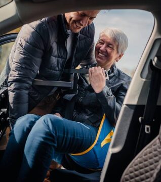 man using a person hoist to help a woman into the car