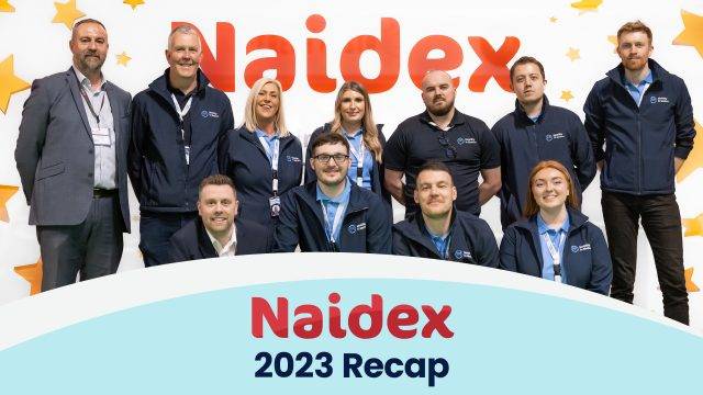 mobility in motion team smiling and standing together in front of naidex 2023 sign