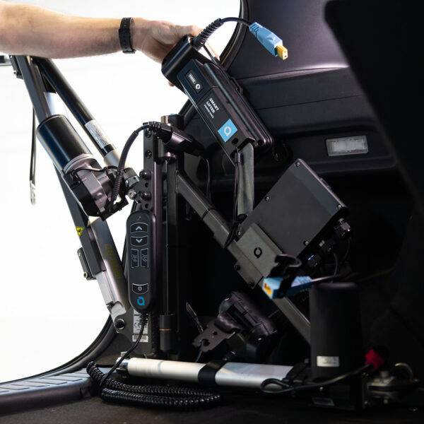 A view looking out the back of a car with its boot open. On the side of the boot. A hand is lowering a Power Pack onto a mounting post on the frame of the boot hoist.