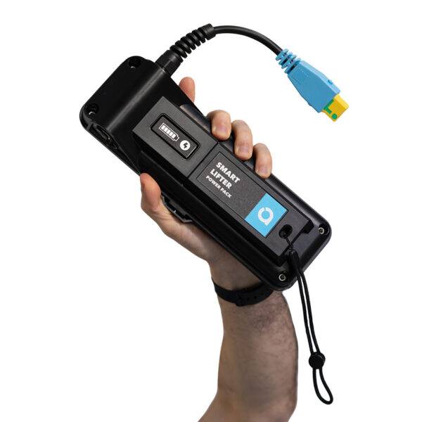 A hand holding up a battery pack for powering a boot hoist. It has a wrist strap and a connector for the boot hoist.