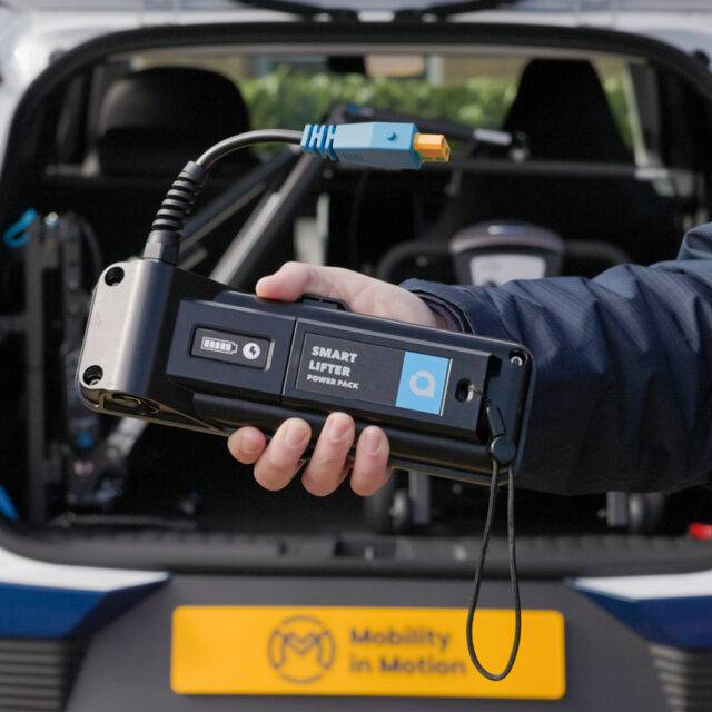 Smart Lifter Power Pack - Battery for Boot Hoists being held in front of the boot of a car