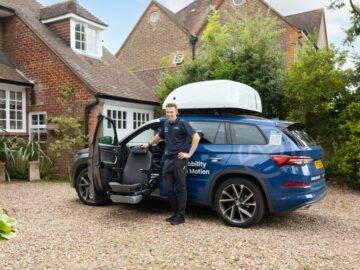 Friendly Mobility in Motion assessor stood smiling next to demo car with wheelchair roof top box and a swivel seat turned out of the front passenger  side