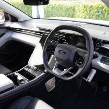 A driver's seat view of the wheel in an EV car with mechanical push/pull hand controls next to the steering wheel