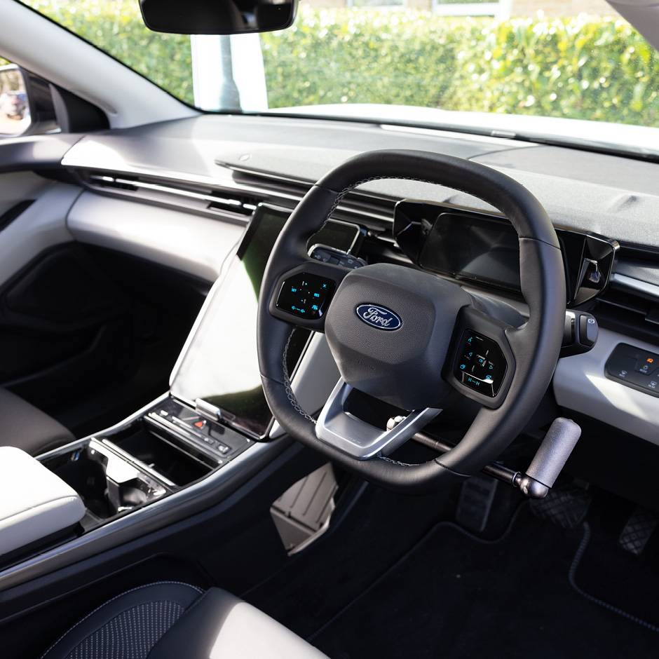 A driver's seat view of the wheel in an EV car with mechanical push/pull hand controls next to the steering wheel