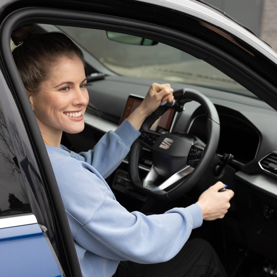 British Paralympian Robyn Love sat in the driver's seat of an adapted car holding the steering wheel with a steering ball and the handle of the hand controls