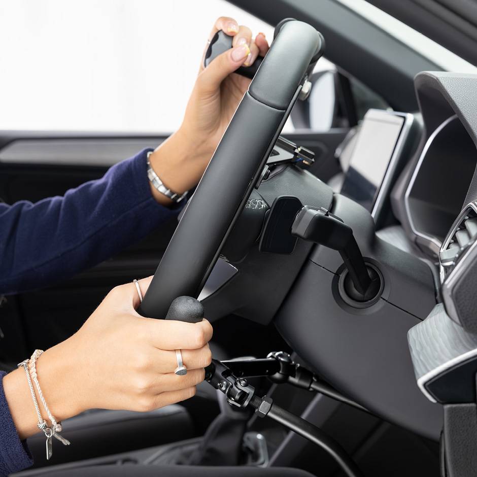 A side view of the steering wheel in an adapted car with mechanical push/pull hand controls next to the steering wheel and a steering ball