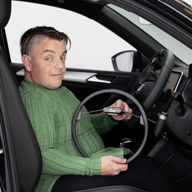 Marcus - The Disabled Reviewer sat in the driver's seat of a car holding an Over Ring Accelerator