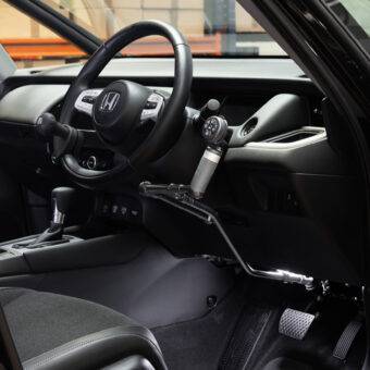 The steering wheel in a car with mechanical push/pull hand controls next to the steering wheel and a remote control keypad above them