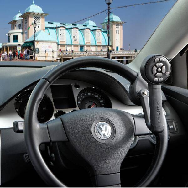 A driver's seat view of the steering wheel in a car with a steering lollipop shaped grip on the steering wheel with a remote control keypad