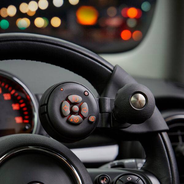 A driver's seat view of the steering wheel in a car with a steering Ball on the steering wheel with a remote control keypad