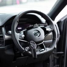 A driver's seat view of the steering wheel in a car with a steering aid on the steering wheel with a remote control keypad