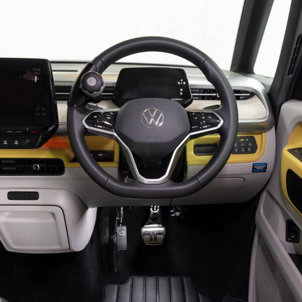 A driver's seat view of a car interior. There is a steering ball on the steering whee. In the footwell the accelerator is folded up and out of the way, a second accelerator pedal has been folded down to the left of the accelerator pedal.