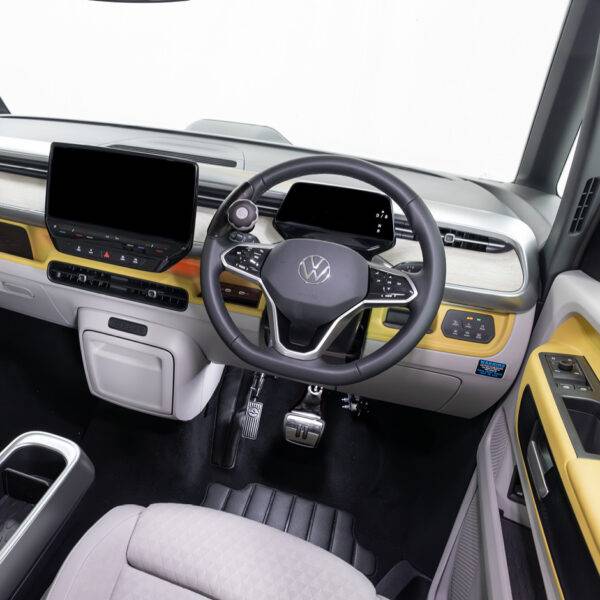 A driver's seat view of a car interior. There is a steering ball on the steering whee. In the footwell the accelerator is folded up and out of the way, a second accelerator pedal has been folded down to the left of the accelerator pedal.