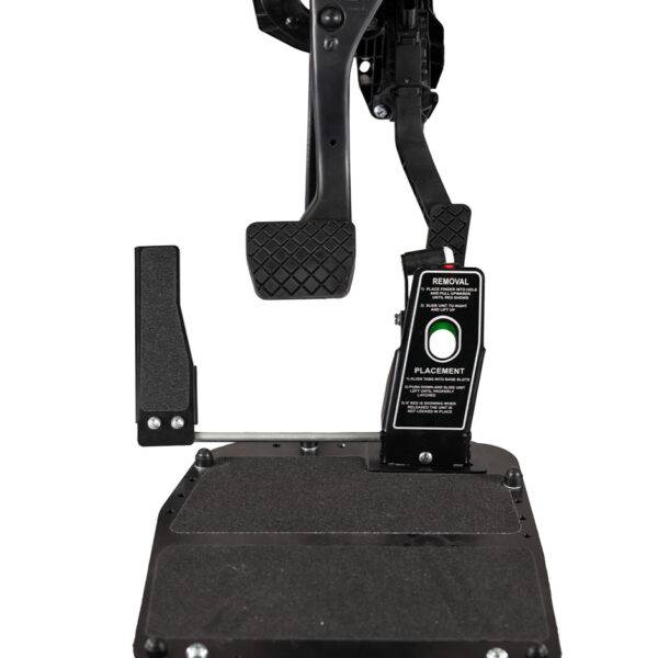 A Left Foot Accelerator Pedal. - A metal plate for the floor of a car's footwell. It is supporting a guard covering the accelerator pedal. Attached to the guard is a second accelerator pedal positioned on the left-hand side of the brake pedal.