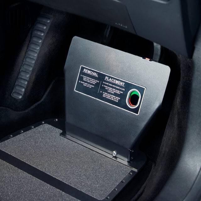 A driver's seat view of a car interior. The car is fitted with hand controls. In the footwell, a metal plate is supporting a guard to cover and protect the car's pedals.