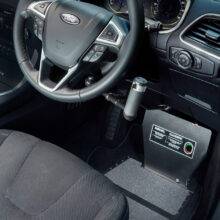 A driver's seat view of a car interior. The car is fitted with hand controls. In the footwell, a metal plate is supporting a guard to cover and protect the car's pedals.