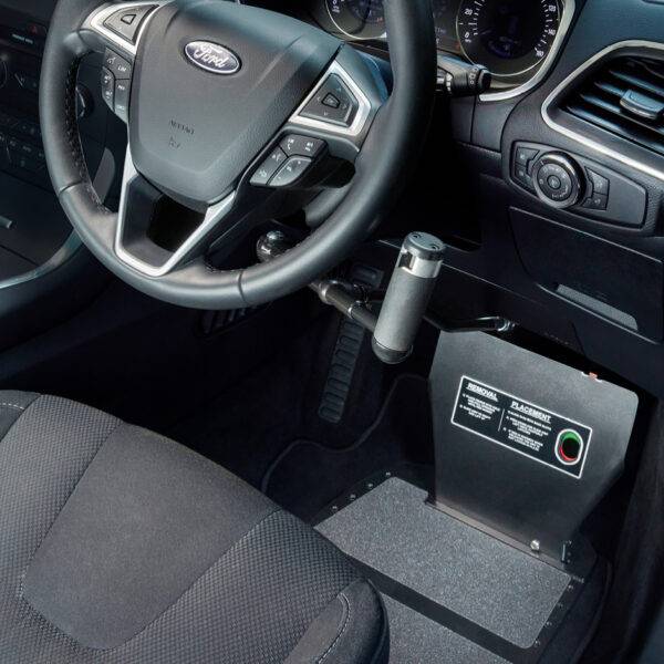 A driver's seat view of a car interior. The car is fitted with hand controls. In the footwell, a metal plate is supporting a guard to cover and protect the car's pedals.