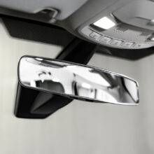 The interior of a car showing a panoramic rear view mirror attached over the top of the car's original mirror. It is wider than a traditional rear view mirror.