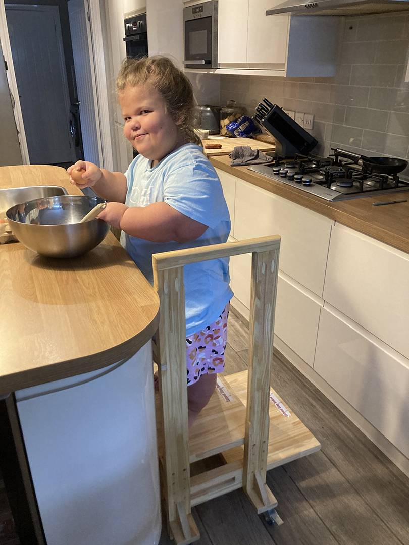 A young person with a mixing bowl is standing on a bespoke wooden step platform made by REMAP.