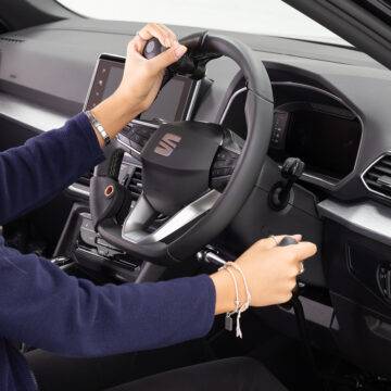 A driver's seat view of the wheel in an adapted car with mechanical push/pull hand controls next to the steering wheel and a steering ball