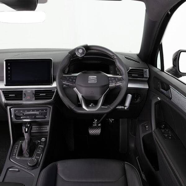 A driver's seat view of the wheel in an adapted car with mechanical push/pull hand controls next to the steering wheel and a steering ball