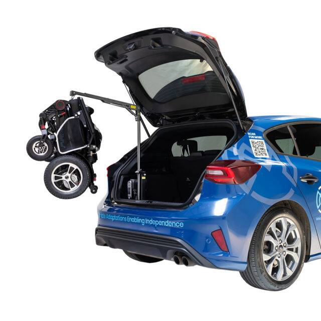 The boot of a Ford Focus with the Brig-Ayd 40kg Boot Hoist, a tall, slender, folding and collapsible hoist arm with a green lifting cord and clip for multiple types of mobility device. It is lifting a folded power chair.