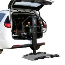 The open boot of a car with the Joey Platform Lift from Bruno. A black and grey metal platform for raising and loading a mobility device into the boot of a vehicle. It had a robust frame a wide adjustable platform.