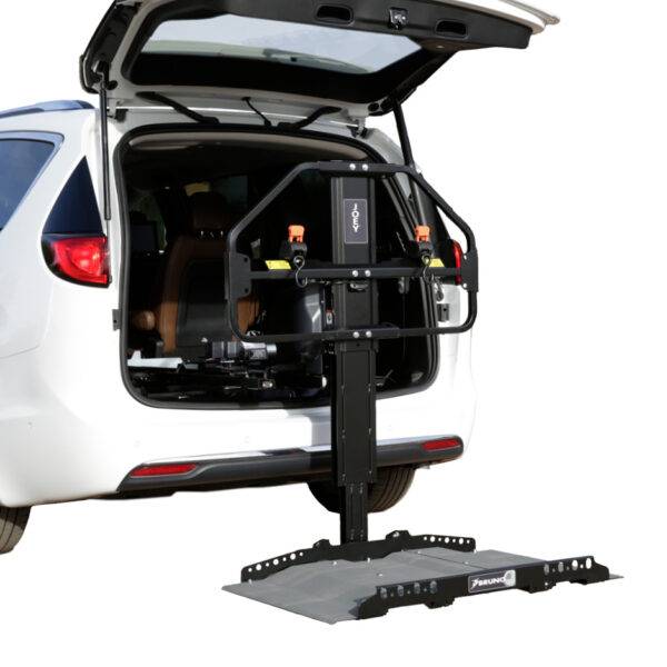 The open boot of a car with the Joey Platform Lift from Bruno. A black and grey metal platform for raising and loading a mobility device into the boot of a vehicle. It had a robust frame a wide adjustable platform.