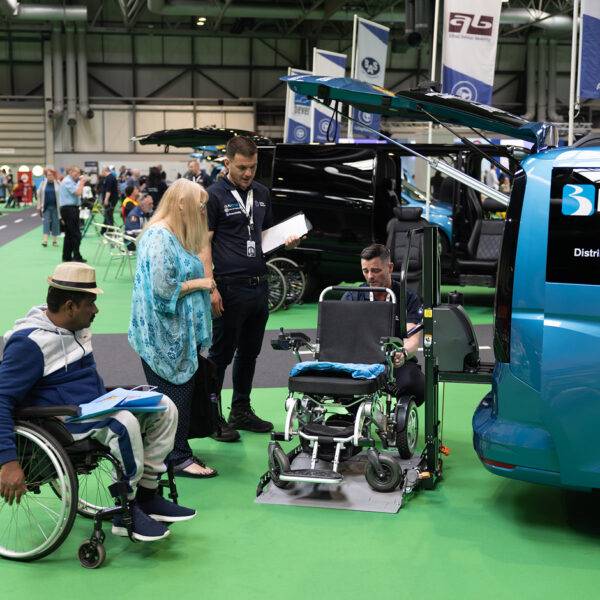 A man in a wheelchair and a woman speaking to the assessors from Mobility in Motion as they measure her power chair to be lifted into the boot of a car by the Joey Platform Lift from Bruno.