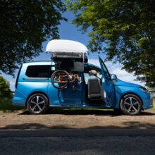 A VW Caddy with a BraunAbility Chair Topper, lowering a folding wheelchair down to the driver's seat, where a Turny Low swivel seat has turned the seat our of the car to bring the driver closer to the wheelchair for an easier transfer