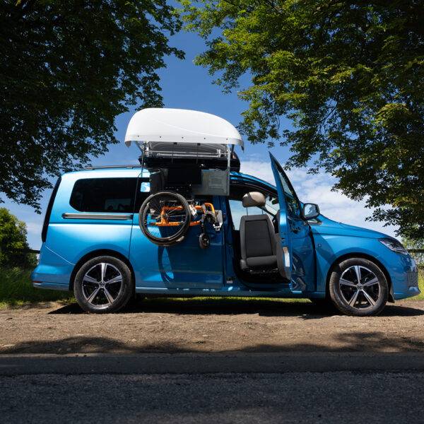 A VW Caddy with a BraunAbility Chair Topper, lowering a folding wheelchair down to the driver's seat, where a Turny Low swivel seat has turned the seat our of the car to bring the driver closer to the wheelchair for an easier transfer