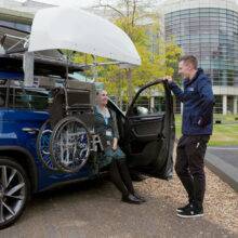 A Mobility in Motion assessor and a young woman lifting a centre folding wheelchair into the roof box of the car with the BraunAbility Chair Topper.