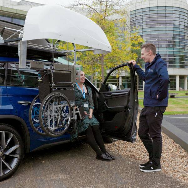 A Mobility in Motion assessor and a young woman lifting a centre folding wheelchair into the roof box of the car with the BraunAbility Chair Topper.