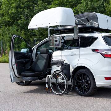 A car with a BraunAbility Chair Topper, lowering a folding wheelchair down to the passenger's seat, where a Turny Evo swivel seat has turned the seat our of the car and lowered it down to bring the passenger closer to the wheelchair for an easier transfer at the ideal height.