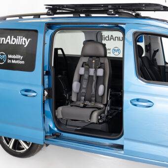 The sliding side door of a car is open to show the Swivel Seat turned out of the car. The BEV Kids seat features a number of additional accessories. It has additional torso support, a lower head rest for a child or someone of smaller stature, as well as a harness. The seat also has a Tilda to allow it to recline and a slide rail allowing it to extend further out of the car for an easier transfer.