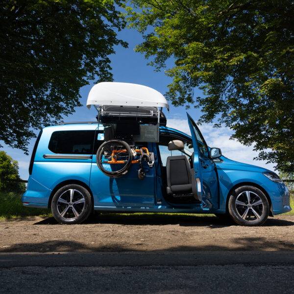 A VW Caddy with a BraunAbility Chair Topper, lowering a folding wheelchair down to the driver's seat, where a Turny Low swivel seat has turned the seat our of the car to bring the driver closer to the wheelchair for an easier transfer