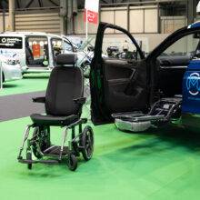 A Mobility in Motion demonstration car with a Carony System wheelchair swivel seat. The car's passenger door is open and the swivel mechanism has turned out and lowered down. Separate from the vehicle, the seat has been transferred onto a wheelchair base.