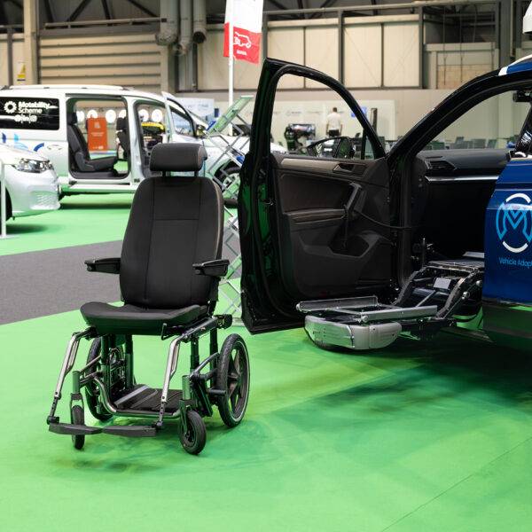 A Mobility in Motion demonstration car with a Carony System wheelchair swivel seat. The car's passenger door is open and the swivel mechanism has turned out and lowered down. Separate from the vehicle, the seat has been transferred onto a wheelchair base.