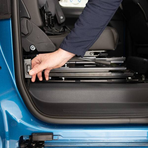 A hand pressing the control switch for the BraunAbility Caroslide Powered Seat Runner on the side of a car's doorframe to move the seat forward or backwards within the car.