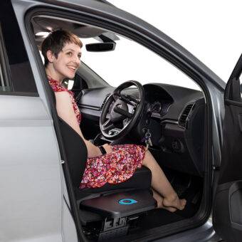 A young woman sat in the driver's seat of her car. The Autochair Transfer Plate is positioned next to the seat of the car.