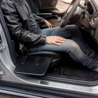 A young man sat in the driver's seat of his car. The BraunAbility Transfer Board is positioned next to the seat of the car.