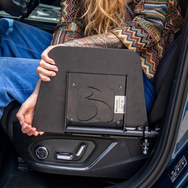 A woman is sat in her car holding the BraunAbility Transfer Board. A small black folding platform positioned next to the passenger seat of the car.