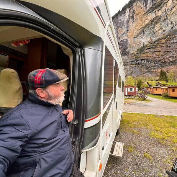 A man sitting on a transfer plate outside the doorframe of his motorhome, looking at the beautiful mountain view beyond.