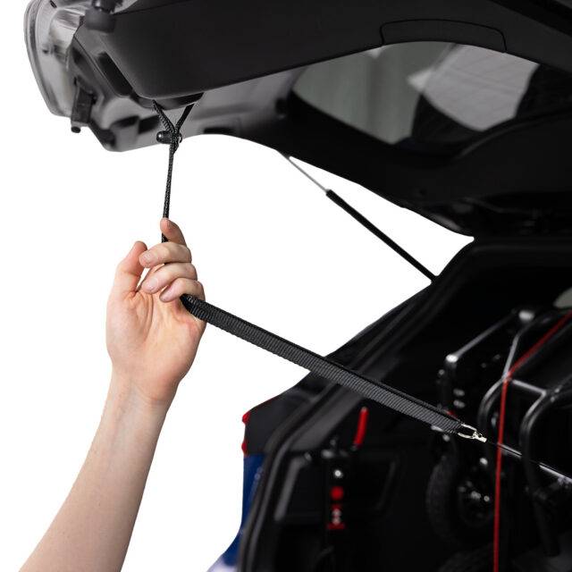 A hand reaching up to grasp a retracting boot strap, a black webbing handle and a subtle retracting mechanism.