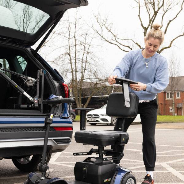 Paralympian Robyn Love at the open boot of a car with a boot hoist, assembling the seat of a mobility scooter. The scooter has the Autochair Smart Scooter seat installed so it can be lifted more easily and fit the vehicle.