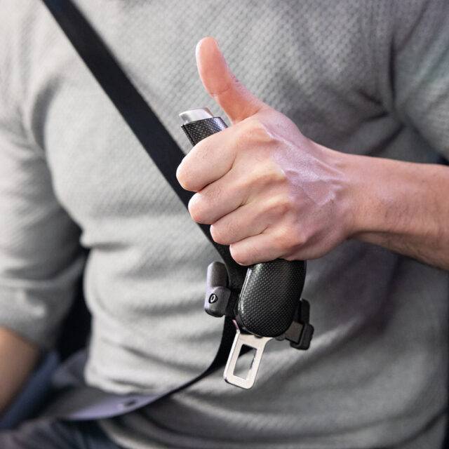 A driver holding their car seatbelt by an additional handle to aid in connecting and unbuckling the belt