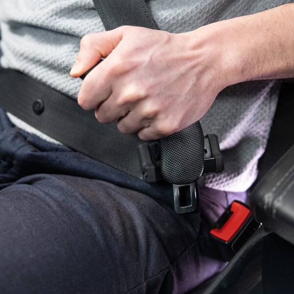 A driver holding their car seatbelt by an additional handle to aid in connecting and unbuckling the belt