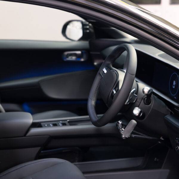 A driver's seat view of the wheel in an EV car with mechanical push/pull hand controls next to the steering wheel.