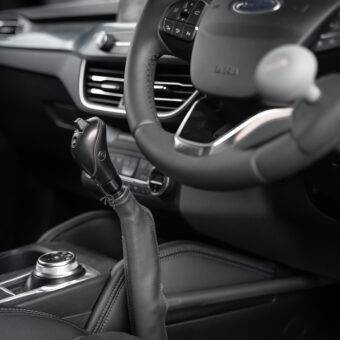 A driver's seat view of the Carospeed Classic, a floor-mounted mechanical push/pull accelerator and brake. A tall black handle with a button on the side to hold the brake. It is positioned for the driver's left hand beside the centre console.